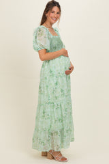 woman wearing a green floral maternity maxi dress with smocked bodice and puff sleeves, showing baby bump