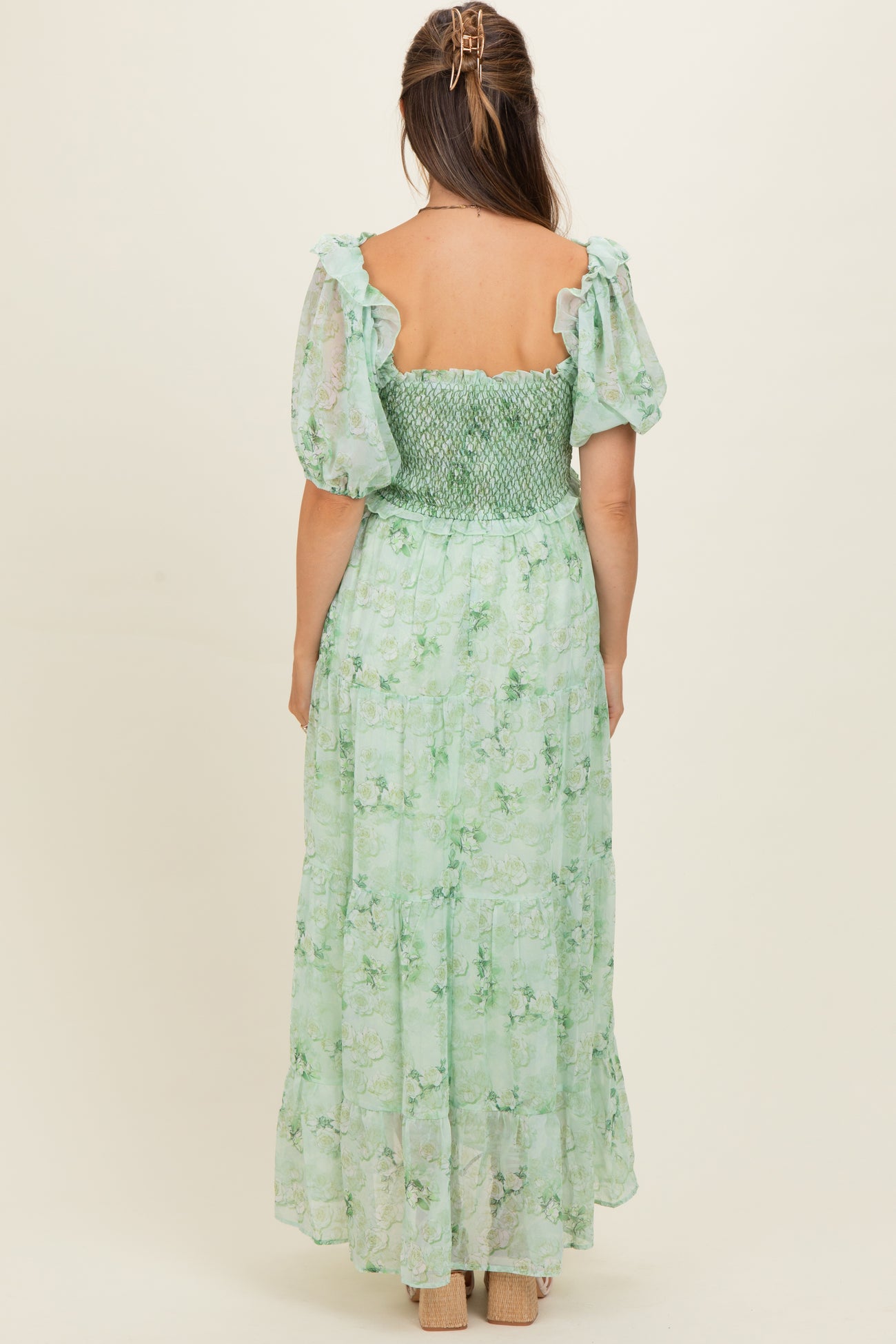 woman wearing a green floral maternity dress with puff sleeves and a smocked bodice, showing the back view