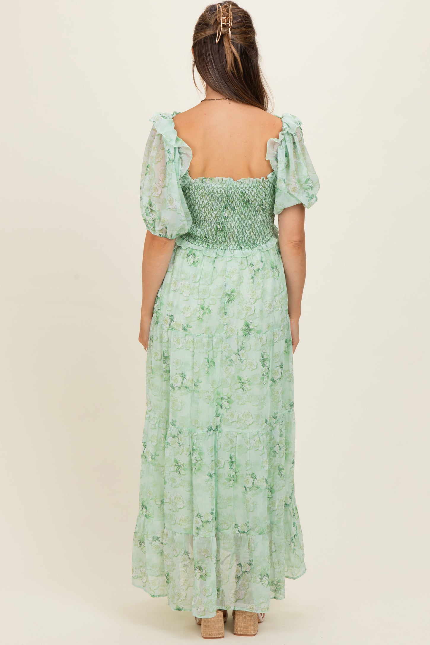 woman wearing a green floral maternity dress with puff sleeves and a smocked bodice, showing the back view