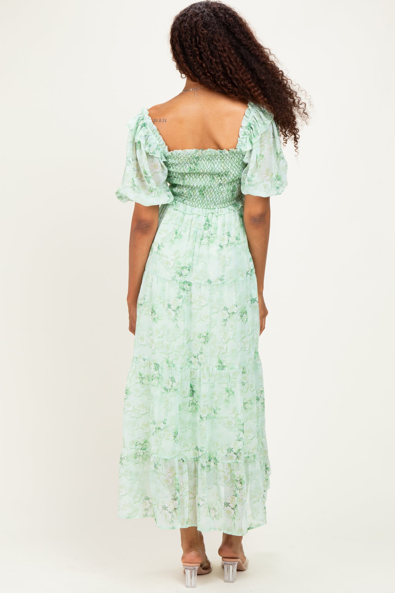 woman wearing a green floral maxi dress with short puff sleeves and a smocked bodice, viewed from the back