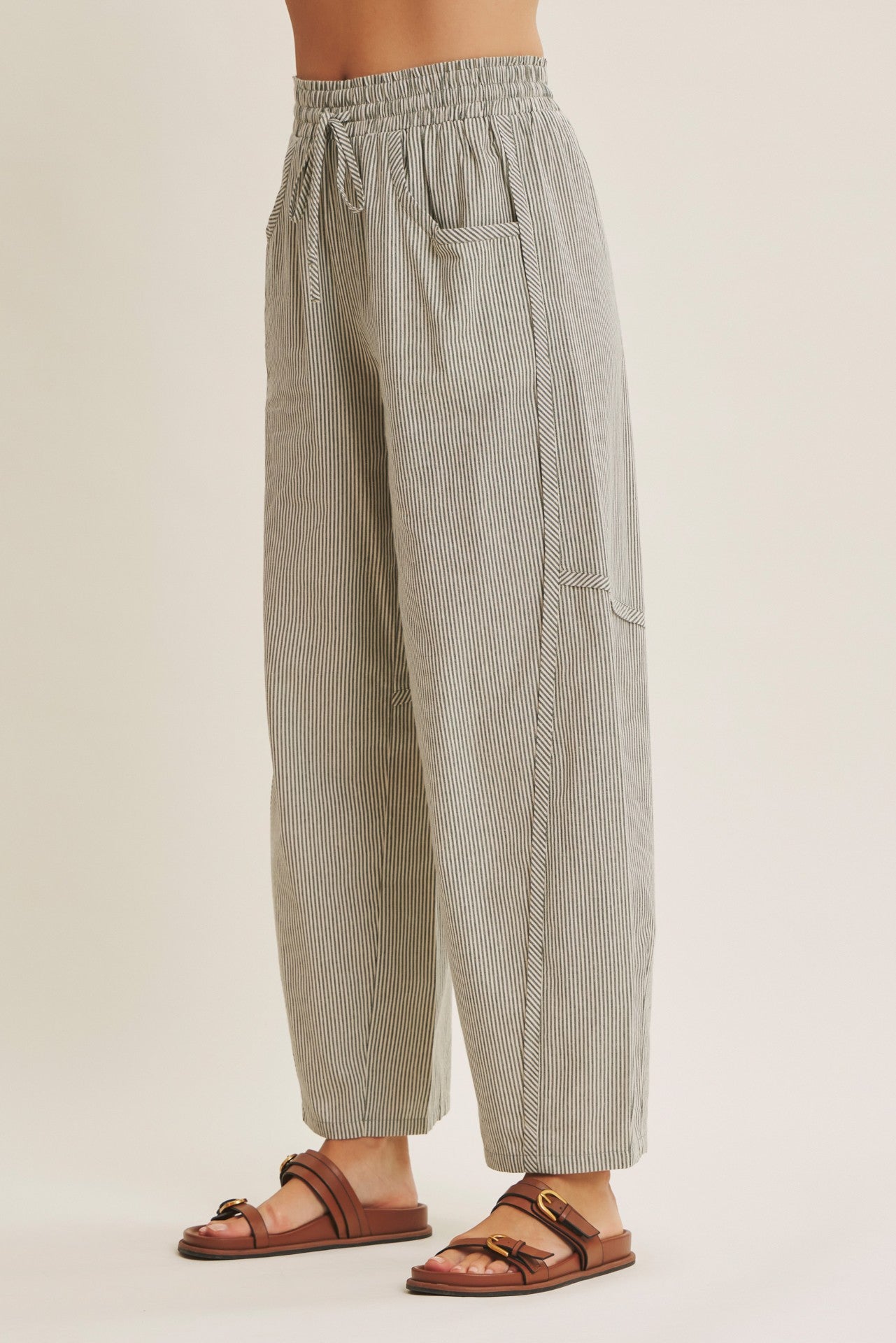 woman wearing black and white striped relaxed fit pants with elastic waistband and side pockets paired with brown sandals