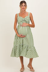 woman wearing a green and white gingham maternity dress with a ruffled hem and holding her baby bump