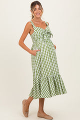 woman wearing a green and white gingham maternity dress with a tie front and ruffled hem, showcasing her baby bump