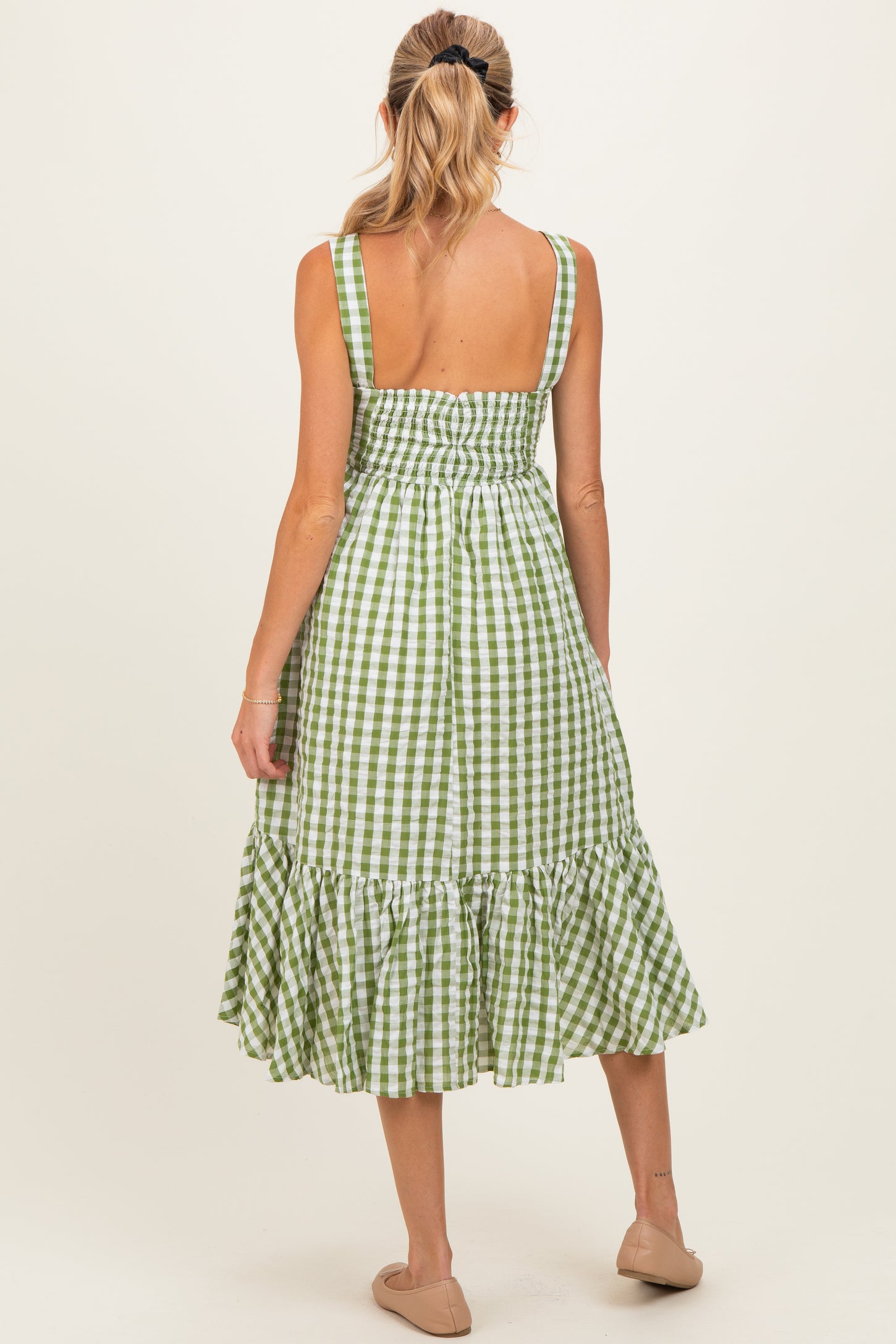 woman wearing a green and white checkered maternity dress with a smocked back and ruffle hem