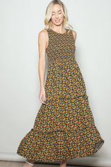 woman wearing a black floral maxi dress with a smocked bodice and tiered skirt, looking down and smiling