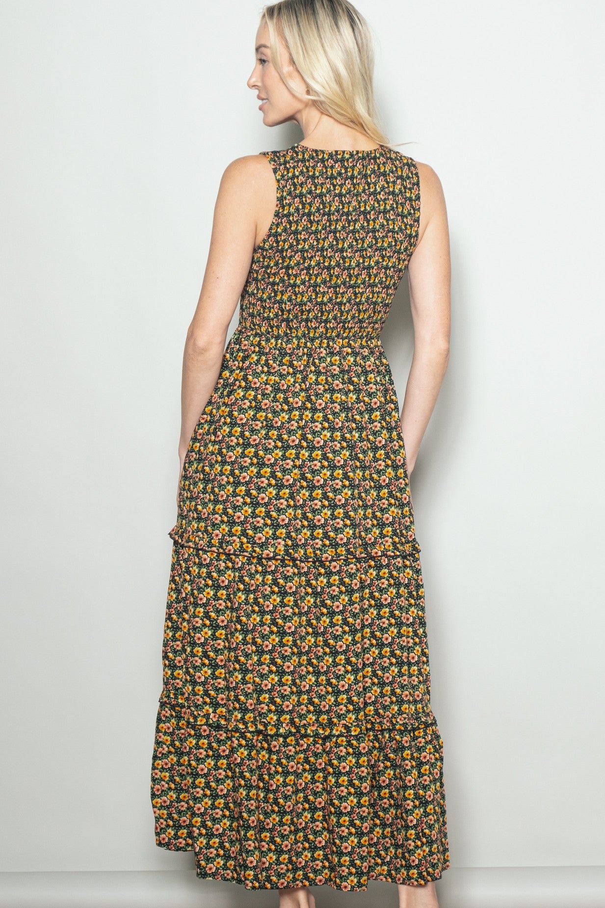 woman wearing a floral print black maxi dress with a tiered skirt and a fitted bodice, viewed from the back