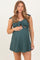 woman wearing a dark green maternity dress with tie straps and cut-out details, holding her baby bump