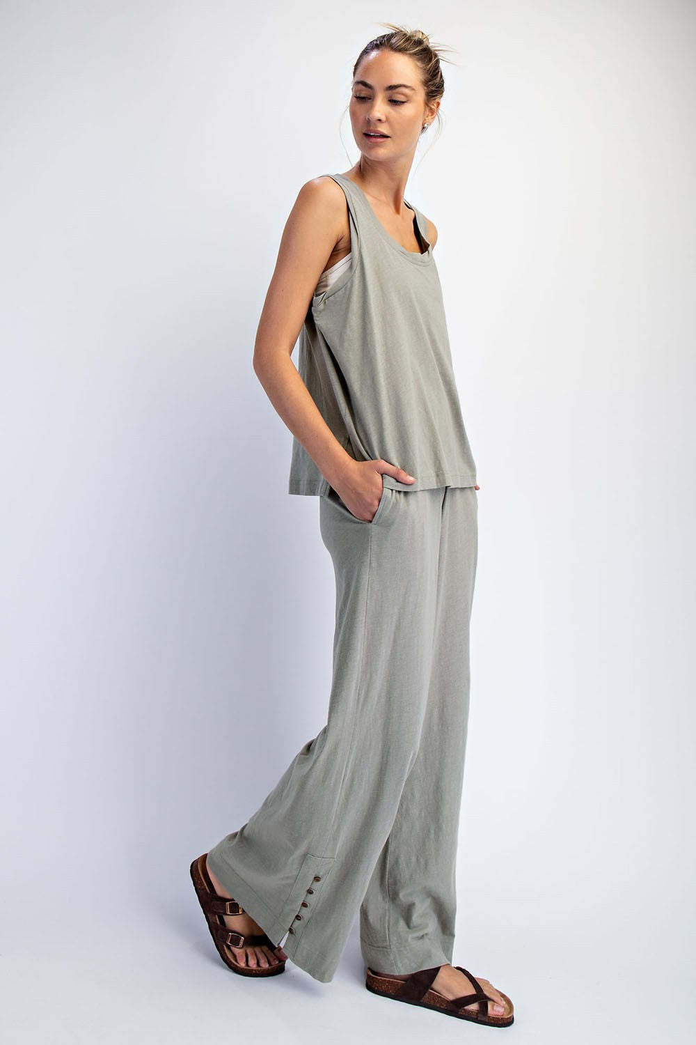 woman wearing a light gray sleeveless top and wide-leg pants with pockets, standing in a relaxed pose