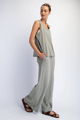 woman wearing a light gray sleeveless top and wide-leg pants with pockets, standing in a relaxed pose