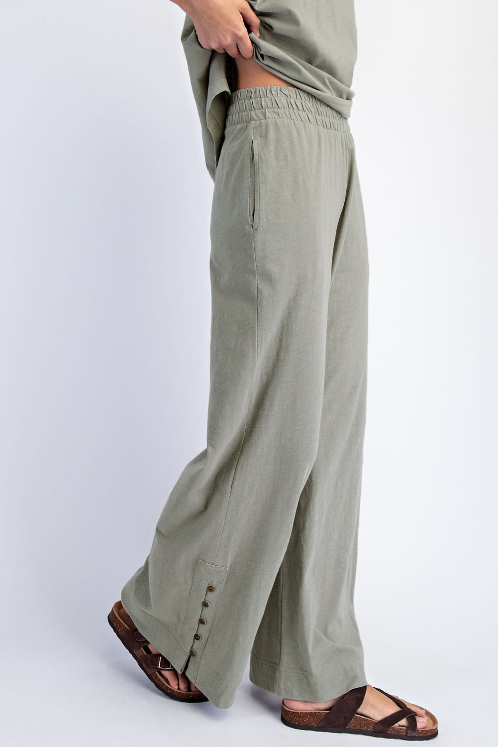 woman wearing olive green wide leg pants with an elastic waistband and side pockets, styled with brown sandals.