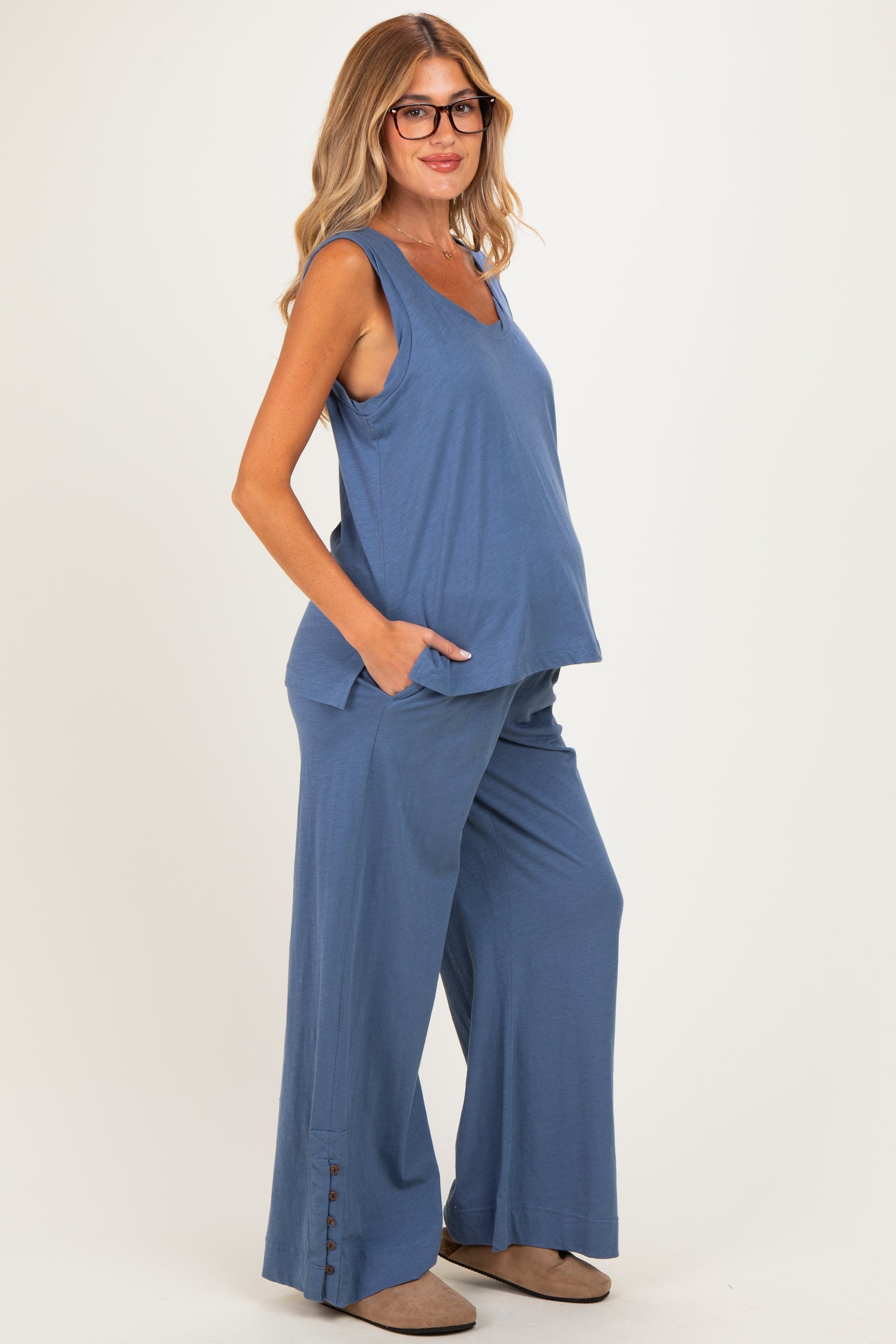 woman wearing a blue maternity tank top and matching wide-leg pants, with a visible baby bump and pockets on the pants