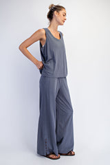 woman wearing a grey sleeveless top and wide leg pants, standing sideways with one hand on hip