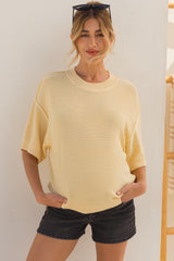 woman wearing a light yellow oversized maternity sweater with short sleeves and distressed black shorts