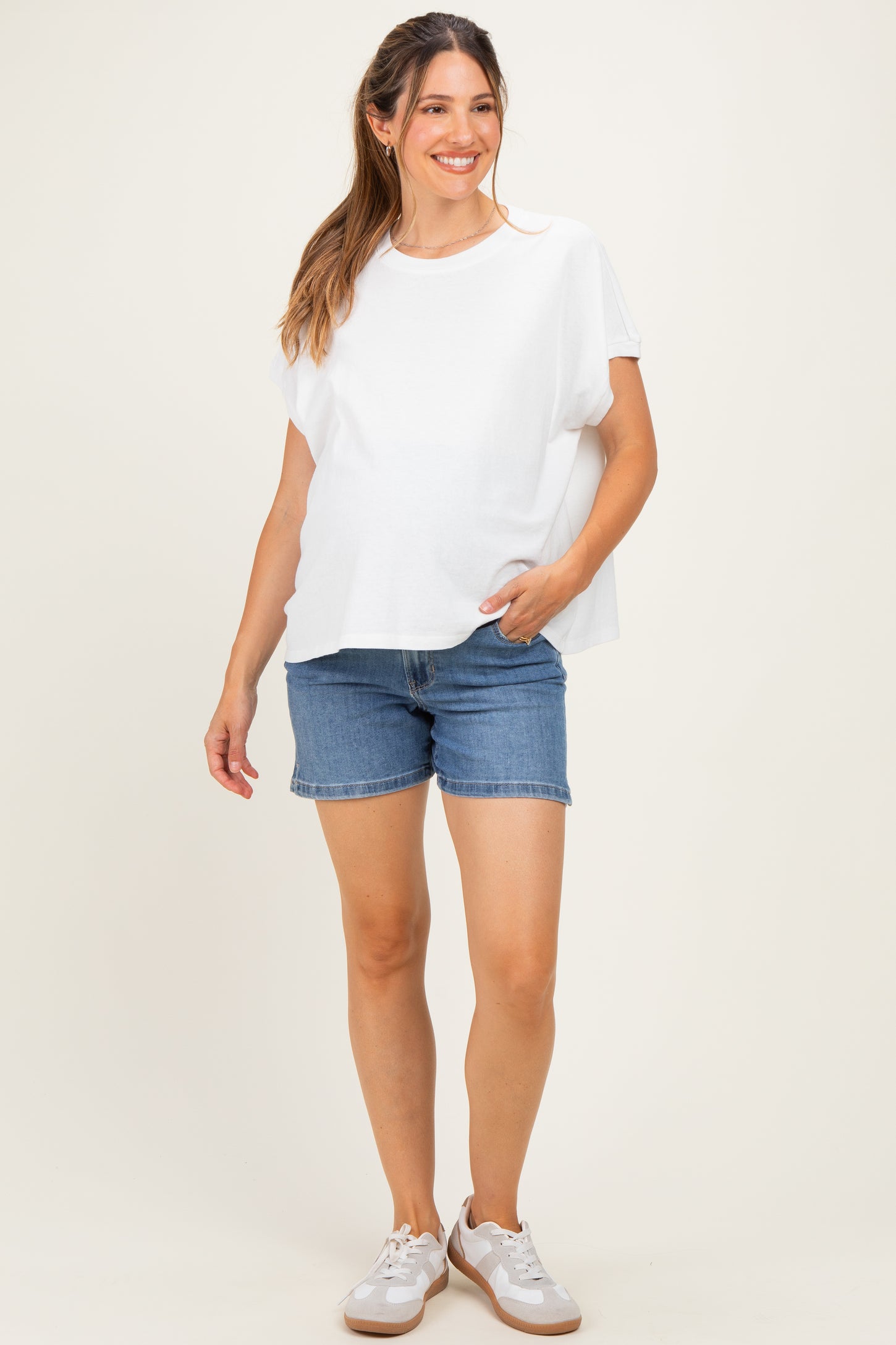 woman wearing a white short sleeve maternity top and denim shorts, showing her baby bump