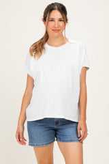 woman wearing a white loose-fitting maternity top and denim shorts, with a visible baby bump