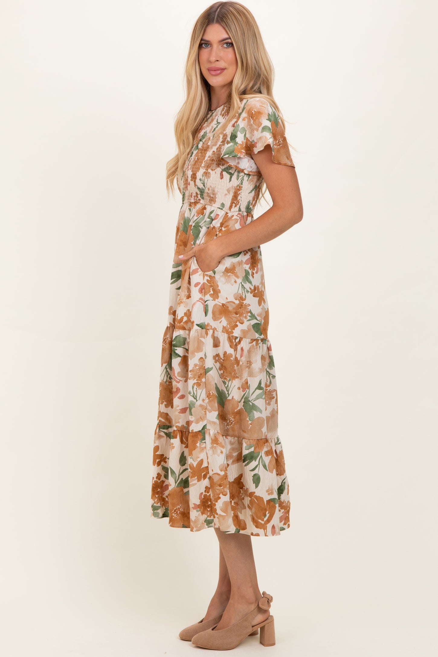 woman wearing a floral midi dress with ruffled sleeves and pockets, model is standing sideways