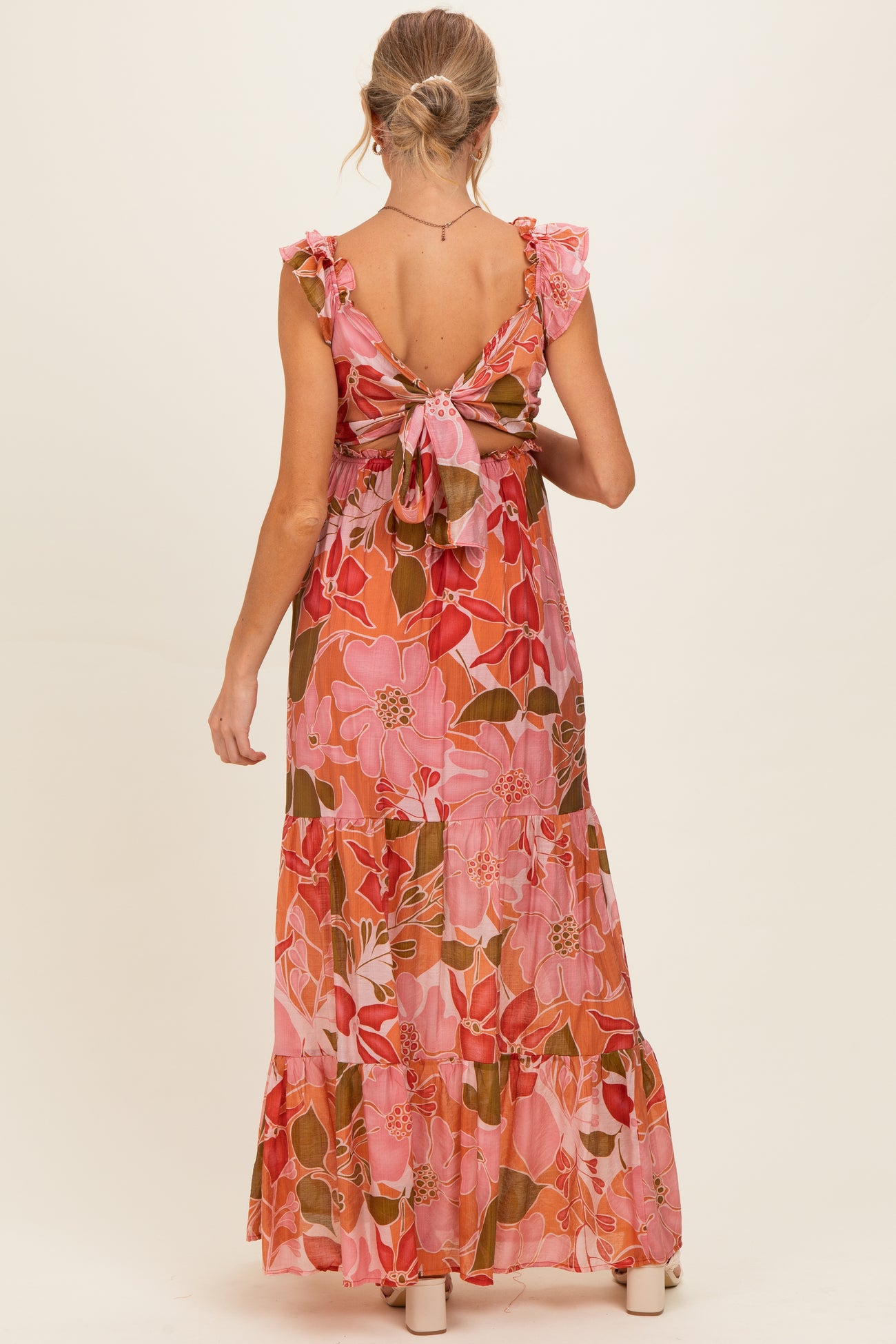 woman wearing a pink floral maternity maxi dress with ruffled sleeves and a tied open back