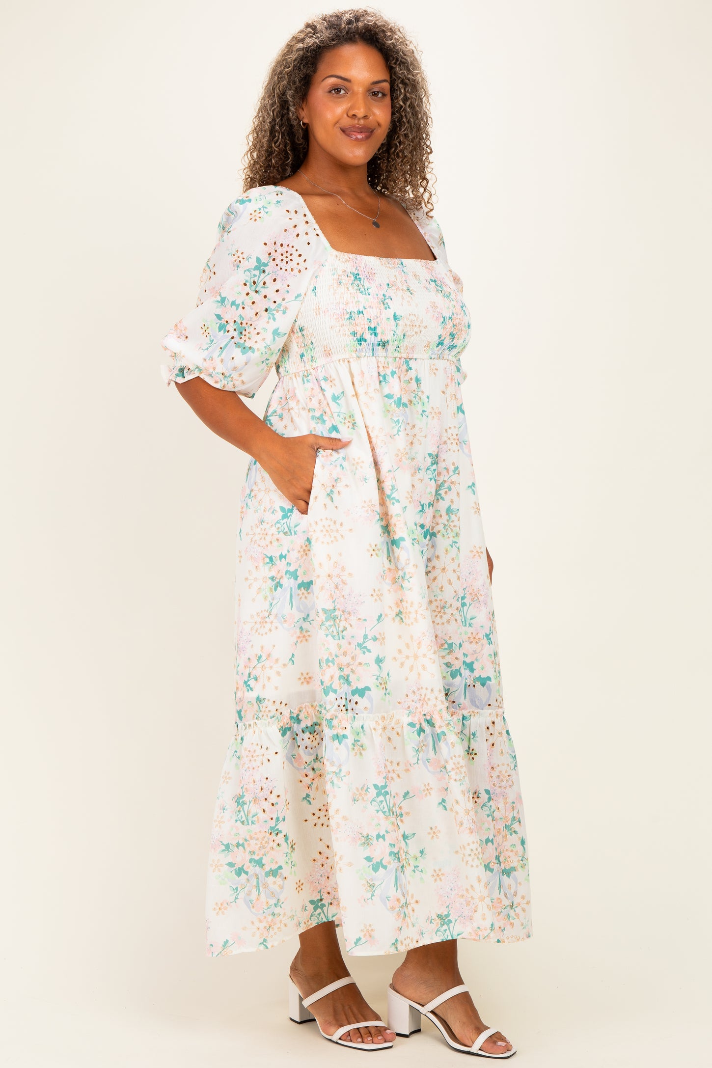 woman wearing a floral plus-size maxi dress with puff sleeves and pockets, standing in a light and airy pose