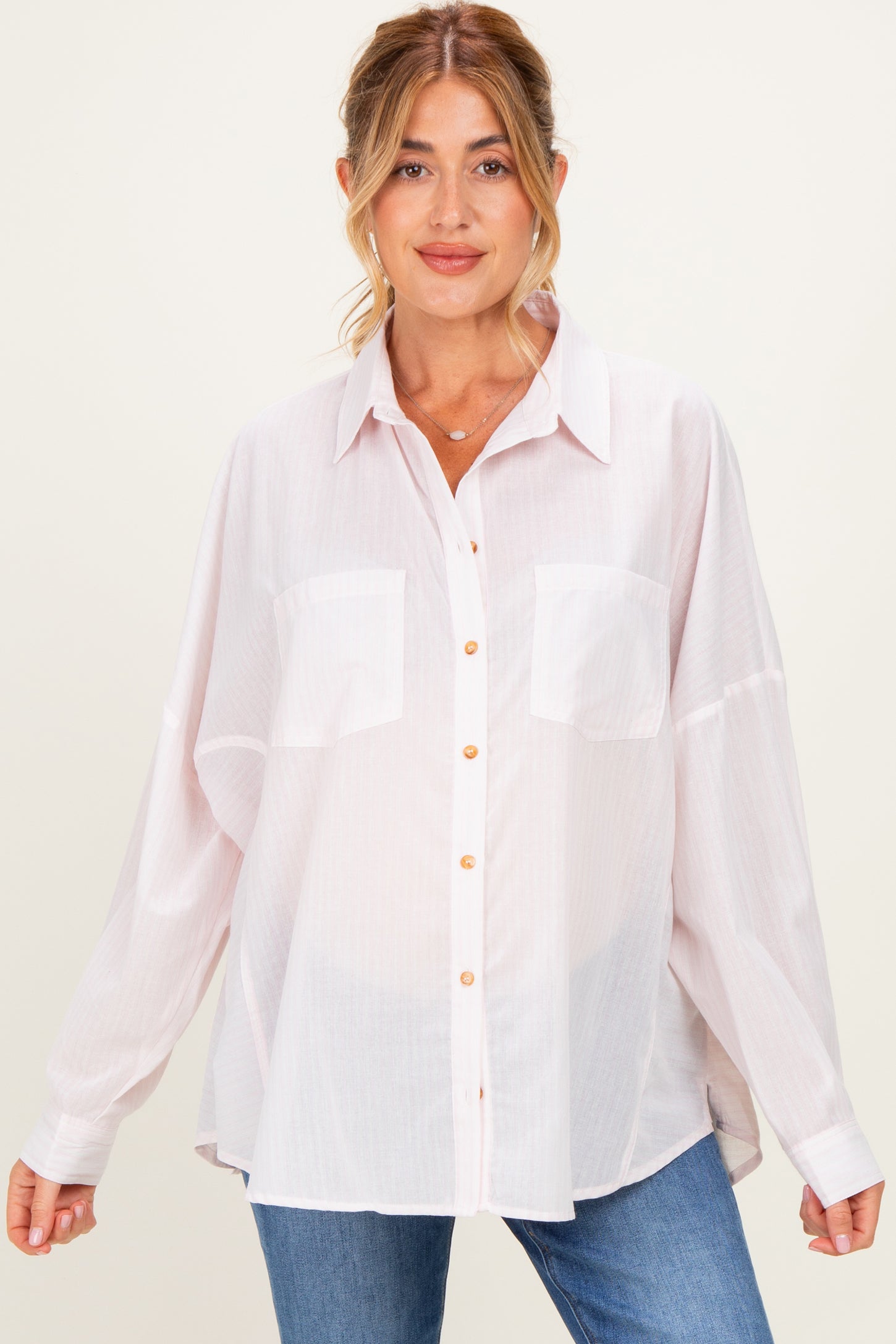 woman wearing a light pink oversized maternity shirt with buttons and breast pockets, styled with blue jeans