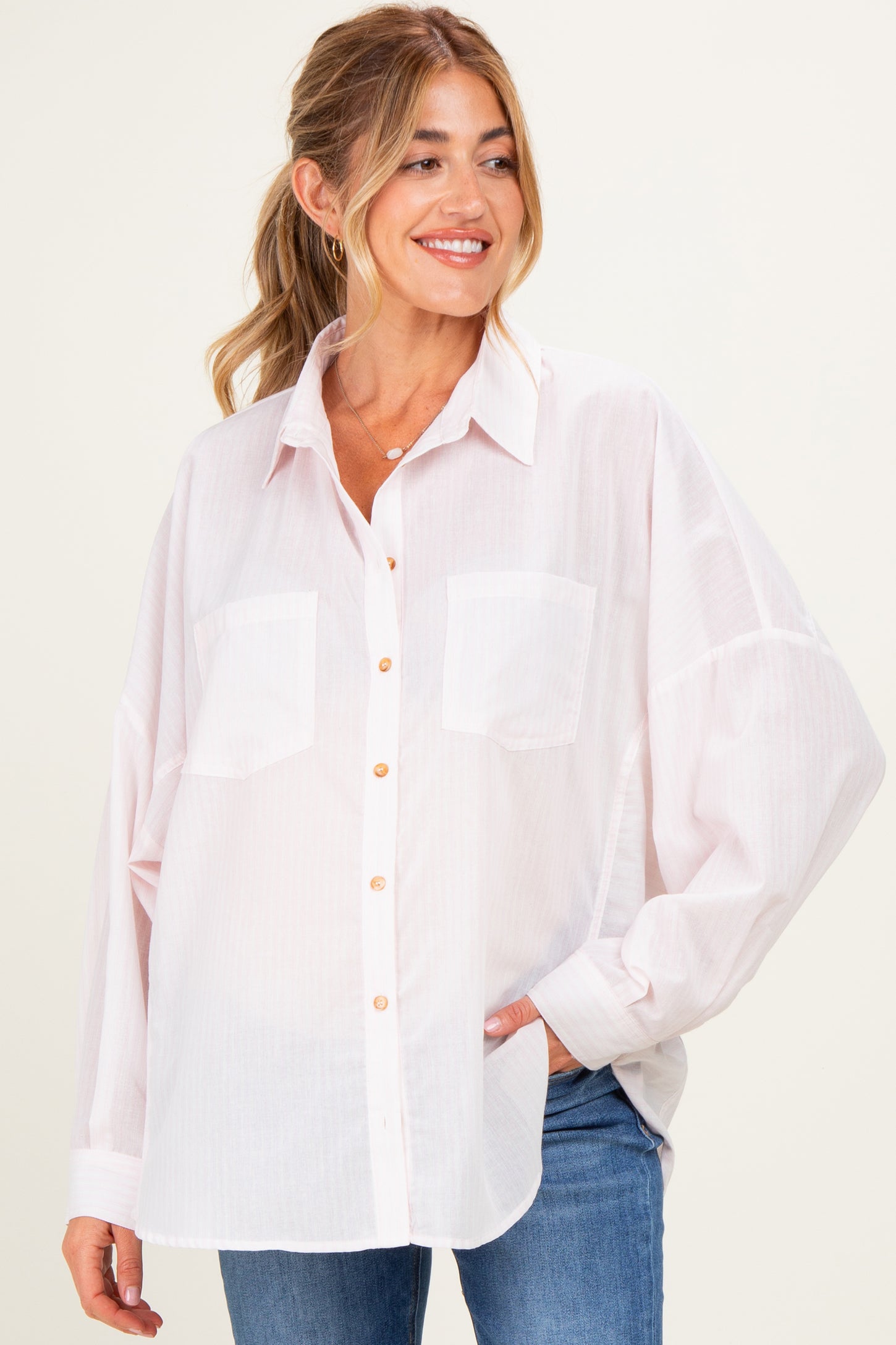 woman wearing a light pink oversized button-up maternity shirt with two chest pockets and rolled sleeves