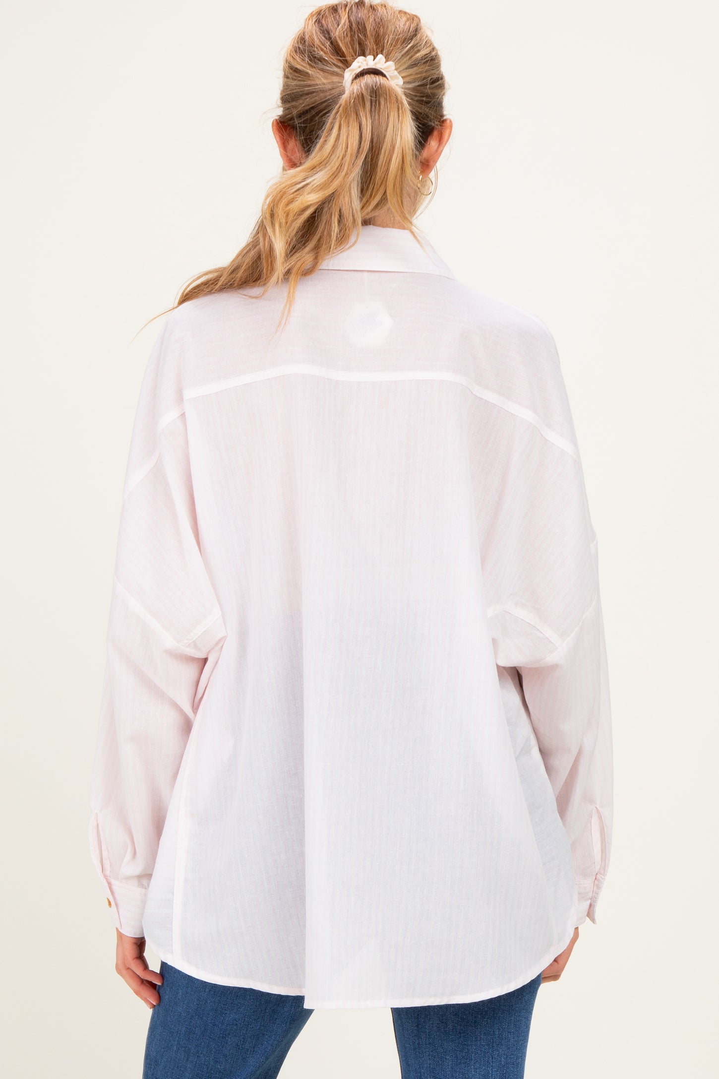 woman wearing a light pink oversized maternity shirt with a button-up back and long sleeves