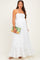 woman wearing a white maternity maxi dress with smocked bodice and tiered ruffle hem, holding a clutch bag and showing her baby bump