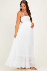 woman wearing a white maternity maxi dress with a smocked bodice and tiered ruffle hem, showing a baby bump
