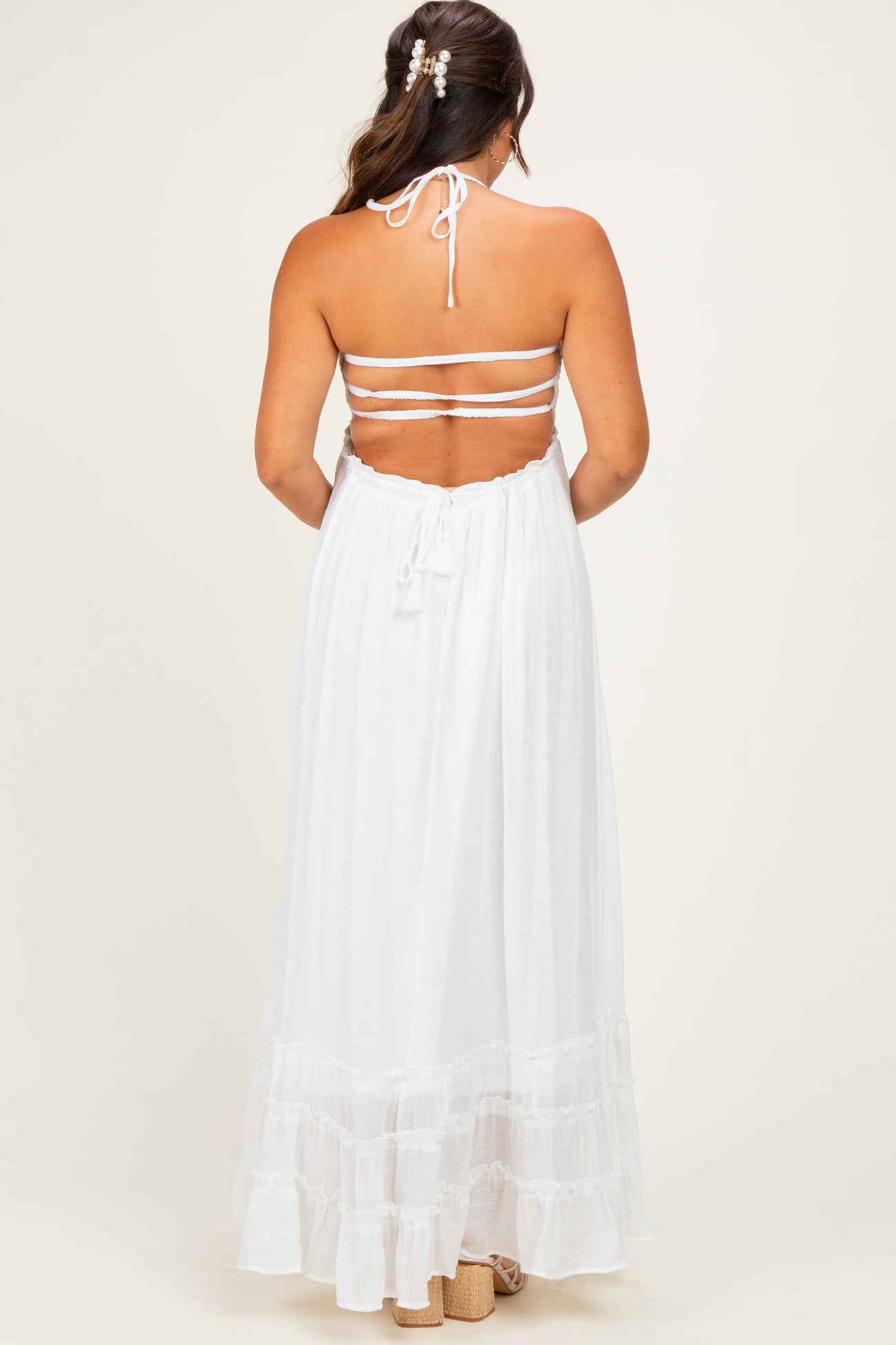 woman wearing a white halter neck maternity maxi dress with tiered ruffle hem and open back design