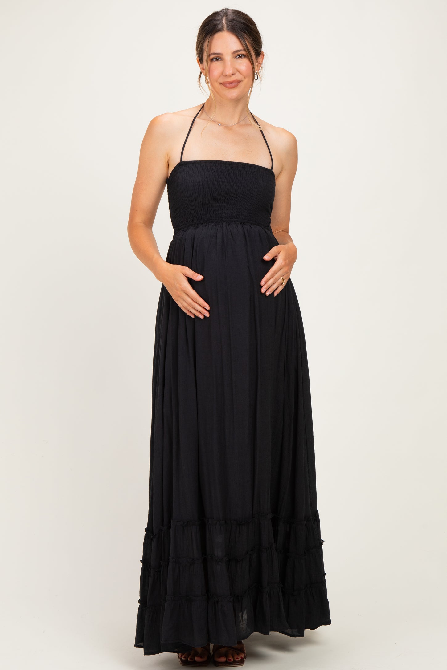 woman wearing a black strapless maxi maternity dress with a smocked bodice and ruffled hem, holding her baby bump