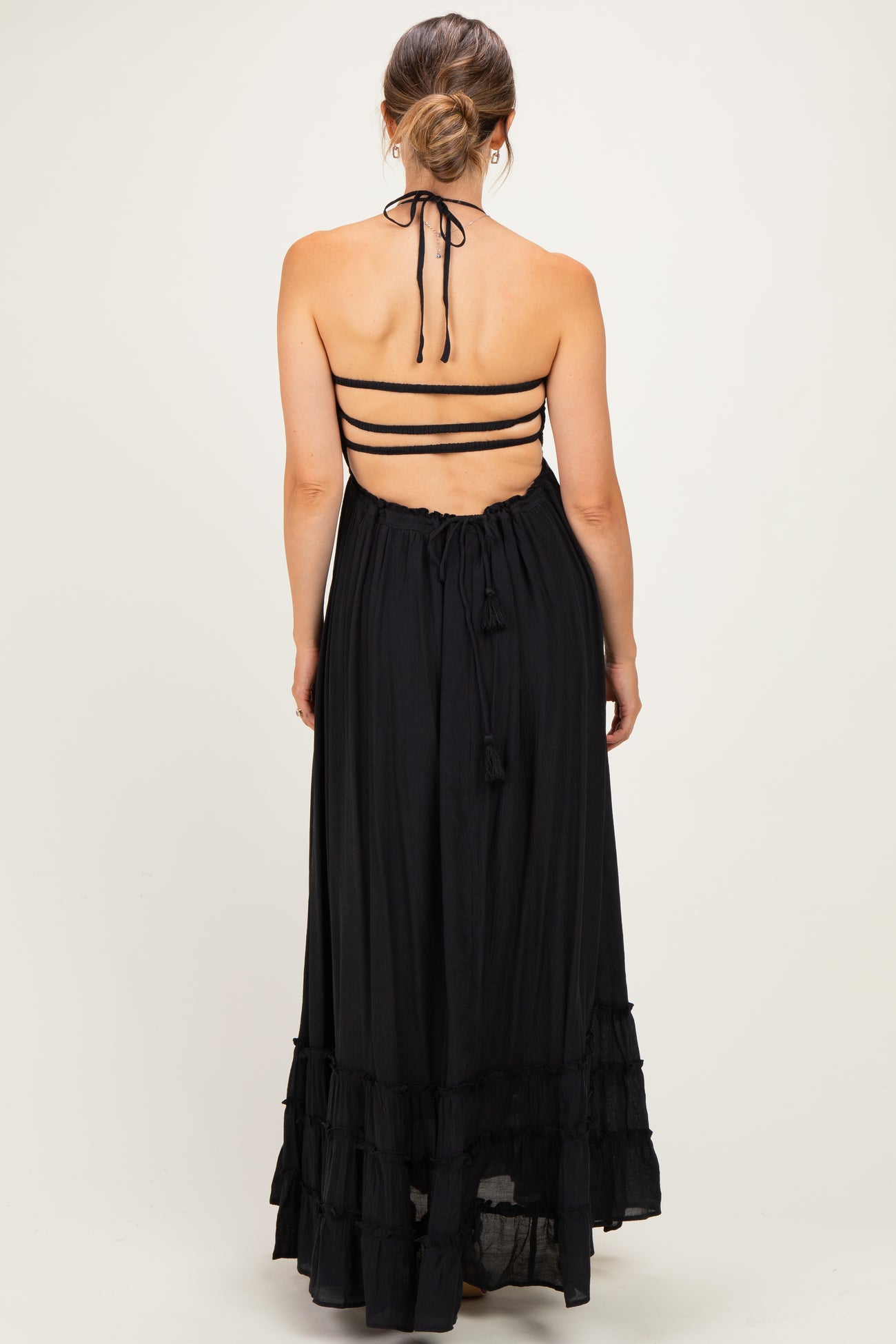 woman wearing a black halter neck maternity maxi dress with adjustable straps and ruffle details, showcasing a baby bump