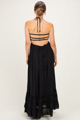woman wearing a black halter neck maternity maxi dress with adjustable straps and ruffle details, showcasing a baby bump