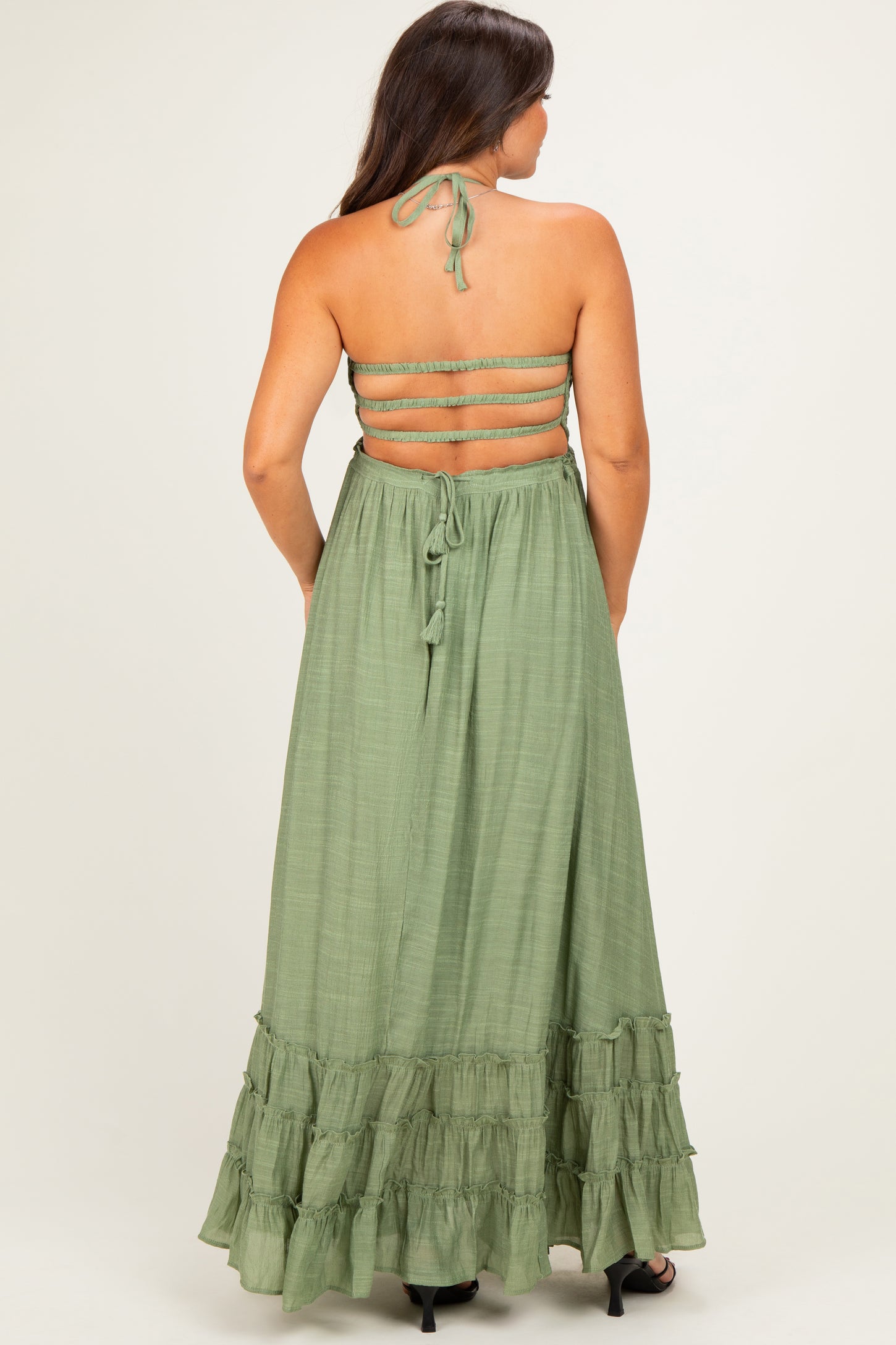 woman wearing a green maternity maxi dress with a tie-back and ruffled hem, showing off her baby bump from the back
