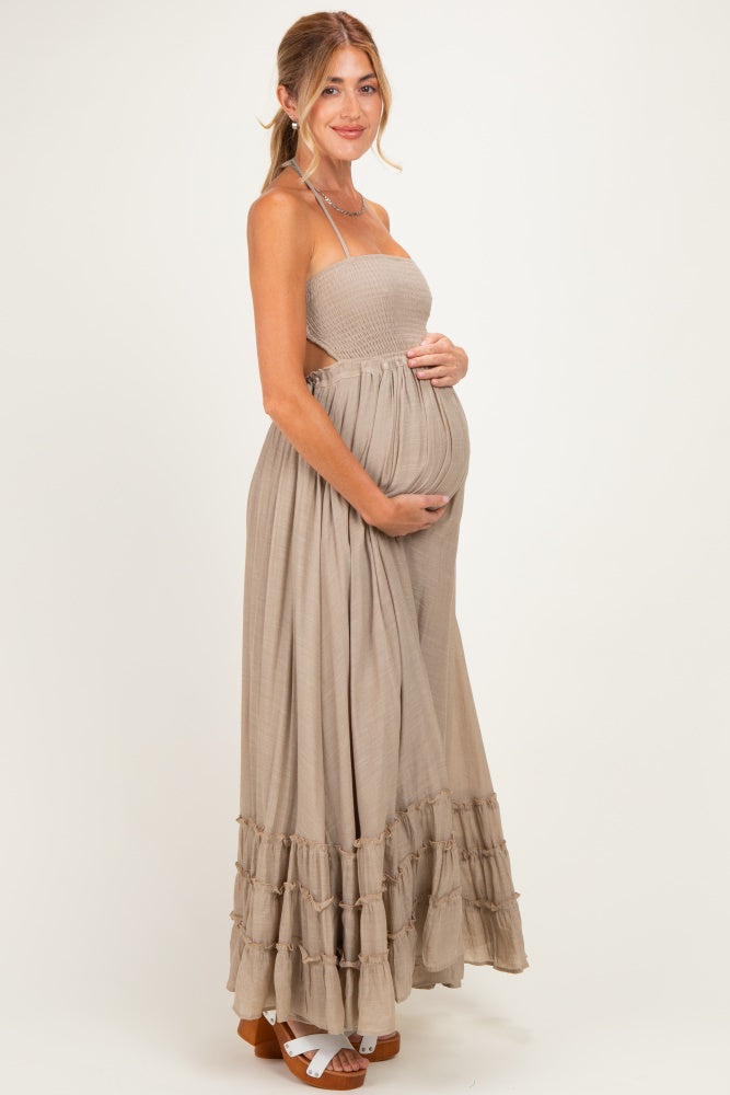 woman wearing a beige maternity maxi dress with a smocked top and tiered ruffle hem, holding her baby bump