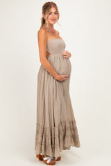 woman wearing a beige maternity maxi dress with a smocked top and tiered ruffle hem, holding her baby bump