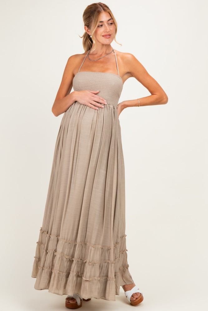 woman wearing a taupe maternity maxi dress with smocked bodice and ruffled hem, gently cradling her baby bump