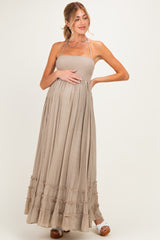 woman wearing a taupe maternity maxi dress with smocked bodice and ruffled hem, gently cradling her baby bump