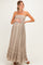 woman wearing a taupe maternity maxi dress with smocked bodice and ruffled hem, gently cradling her baby bump