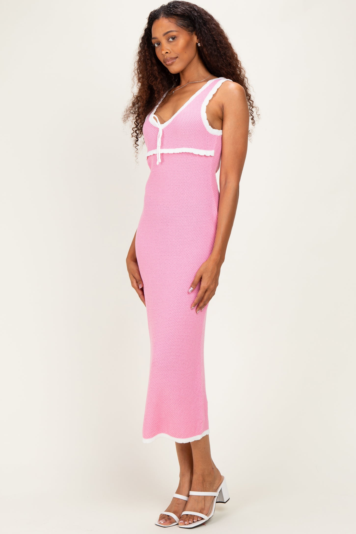 woman wearing a pink knit midi dress with white trim and a spaghetti strap neckline, standing with a slight smile