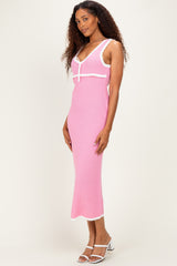 woman wearing a pink knit midi dress with white trim and a spaghetti strap neckline, standing with a slight smile