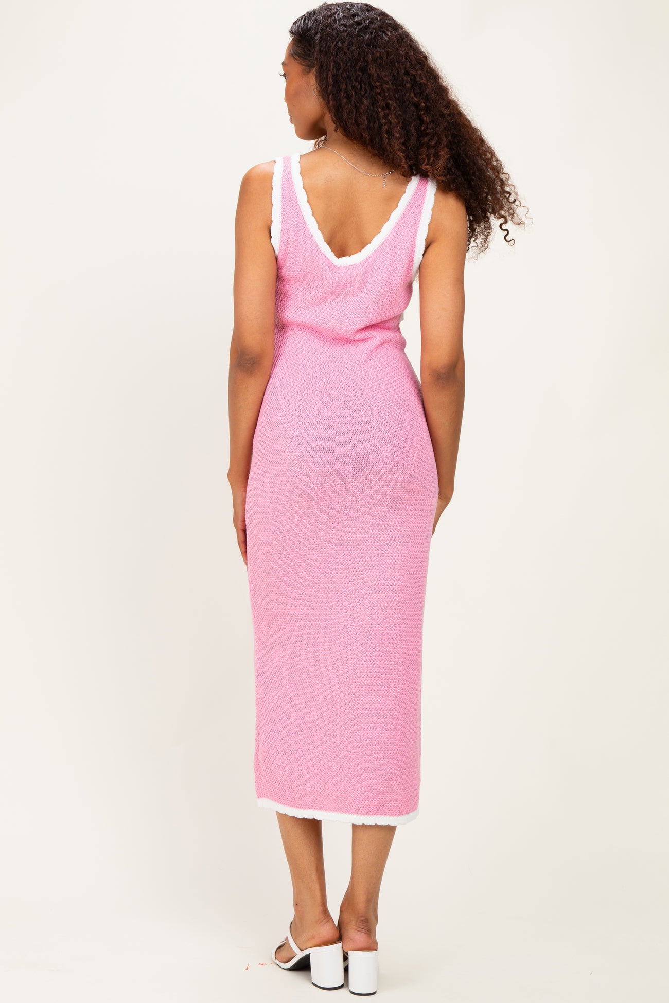 woman wearing a pink sleeveless knit midi dress with white trim, viewed from the back
