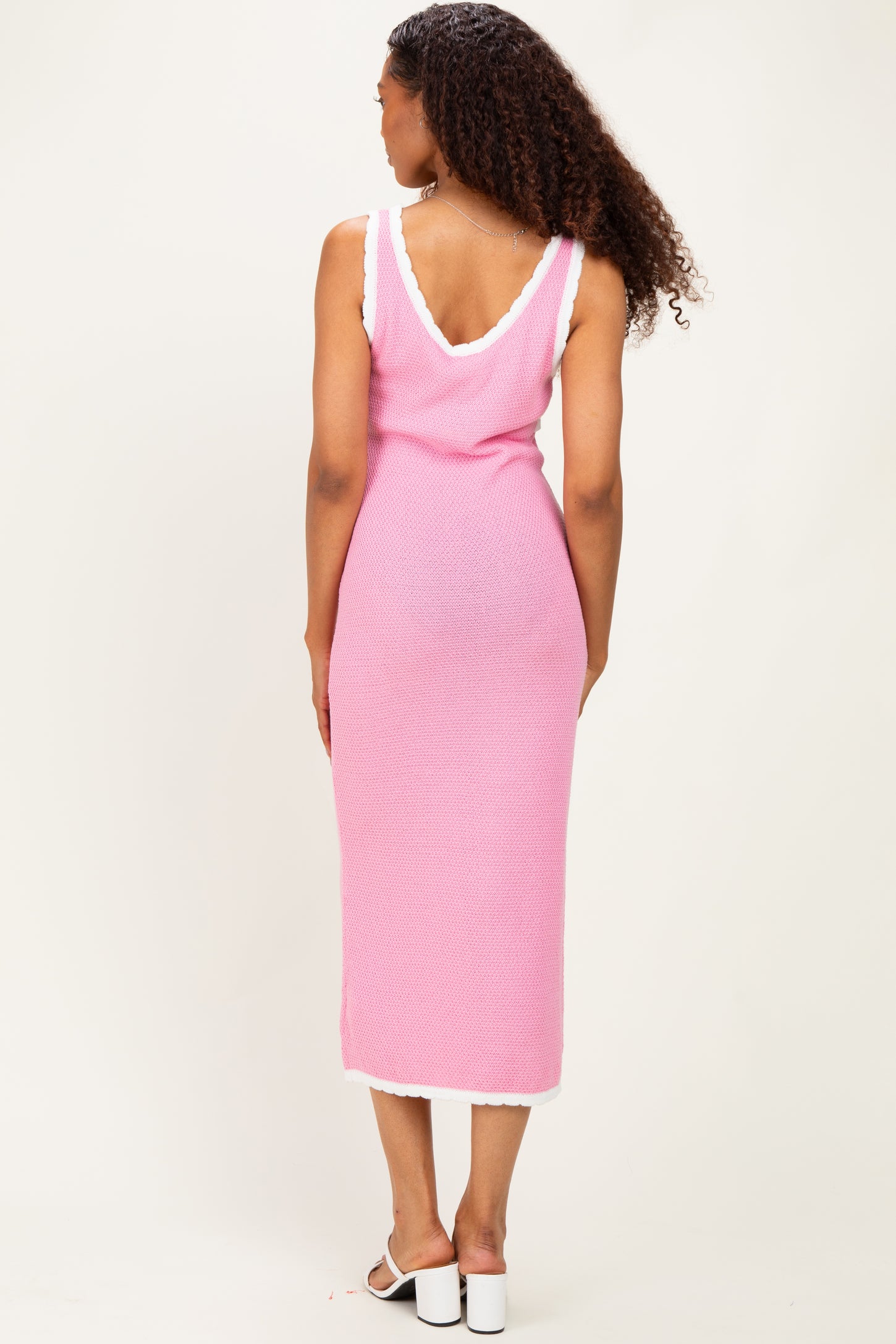 woman wearing a pink sleeveless knit midi dress with white trim, viewed from the back