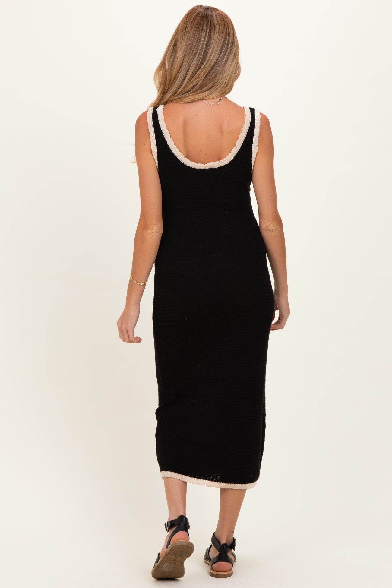 woman wearing a black maternity dress with a cream trim, showing a fitted silhouette and a midi length from the back