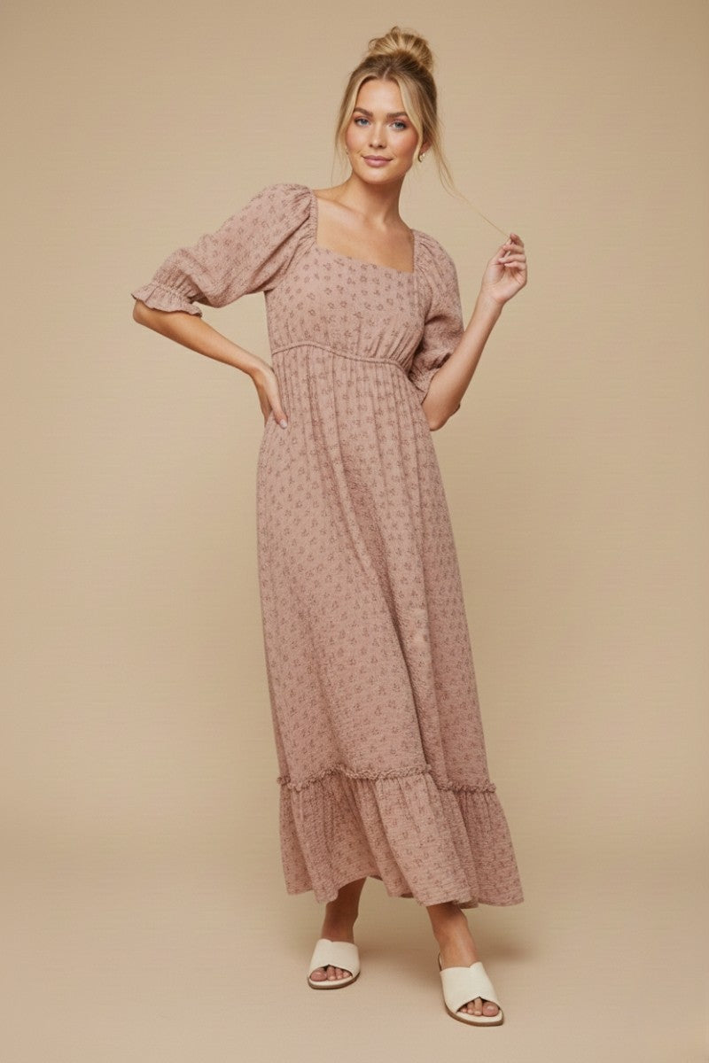 woman wearing a blush pink floral maxi dress with puff sleeves and a tiered hem, standing against a neutral background
