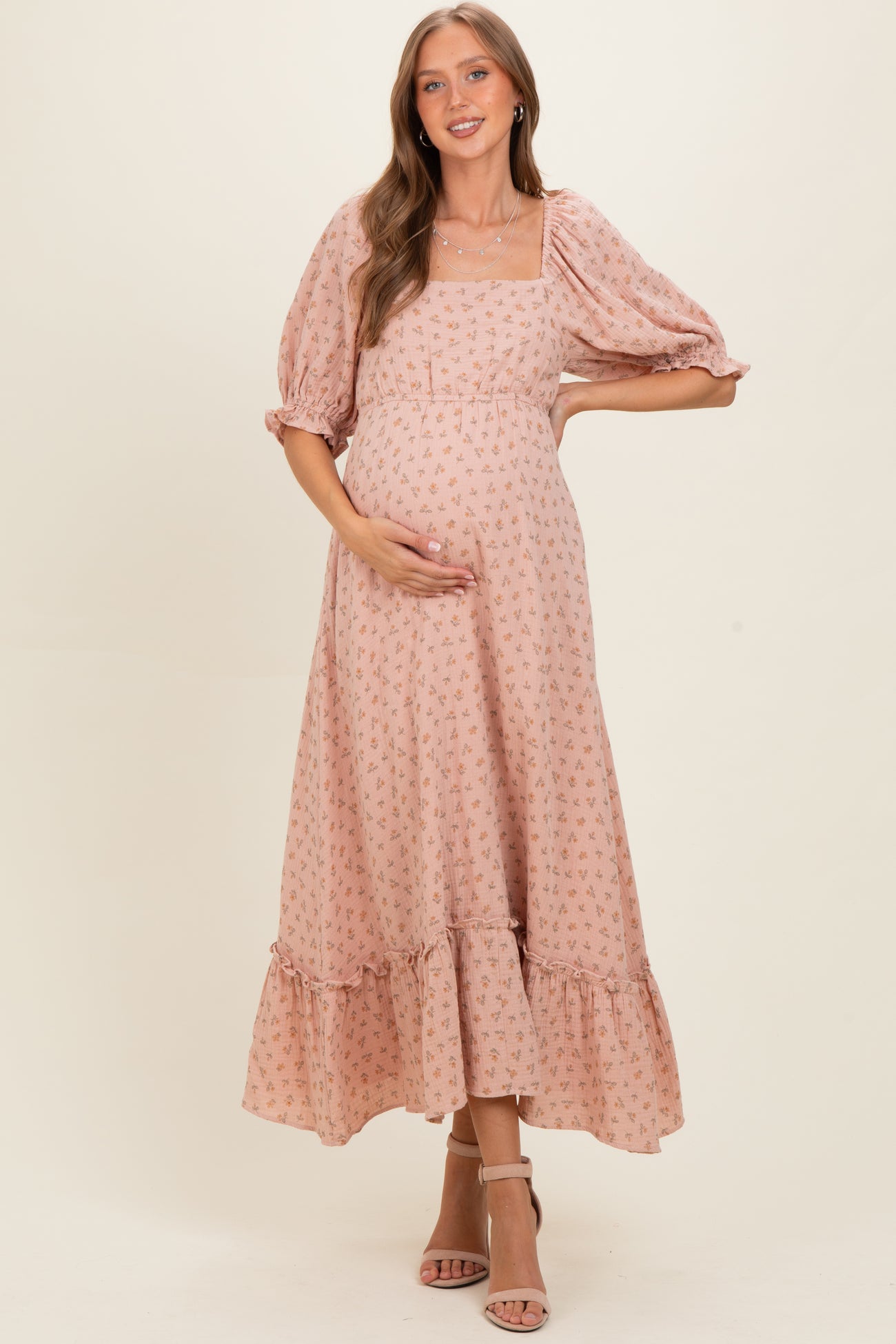 woman wearing a pink floral maternity dress with puff sleeves and a ruffled hem, gently cradling her baby bump