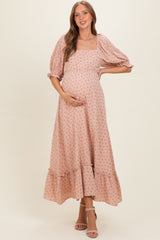 woman wearing a pink floral maternity dress with puff sleeves and a ruffled hem, gently cradling her baby bump