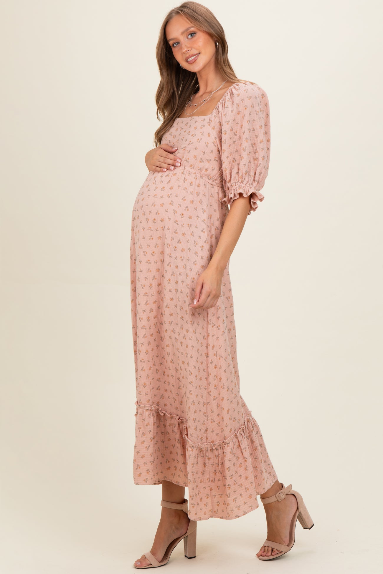 woman wearing a blush pink floral maternity maxi dress with puff sleeves and a ruffled hem, holding her baby bump