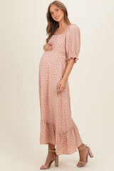 woman wearing a blush pink floral maternity maxi dress with puff sleeves and a ruffled hem, holding her baby bump
