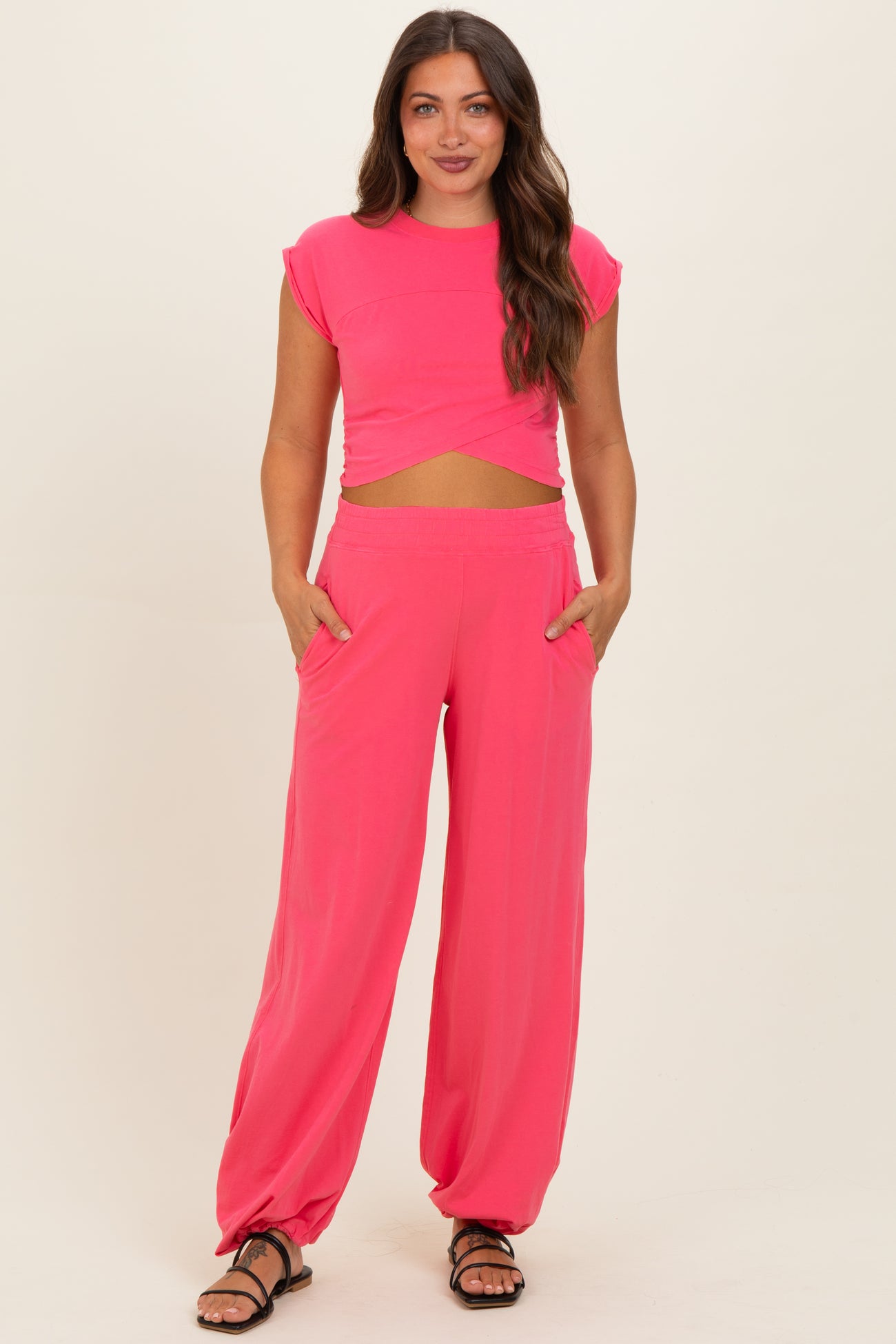 woman wearing a bright pink maternity two-piece set with a cropped top and loose-fitting pants, holding pockets