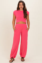 woman wearing a bright pink maternity two-piece set with a cropped top and loose-fitting pants, holding pockets
