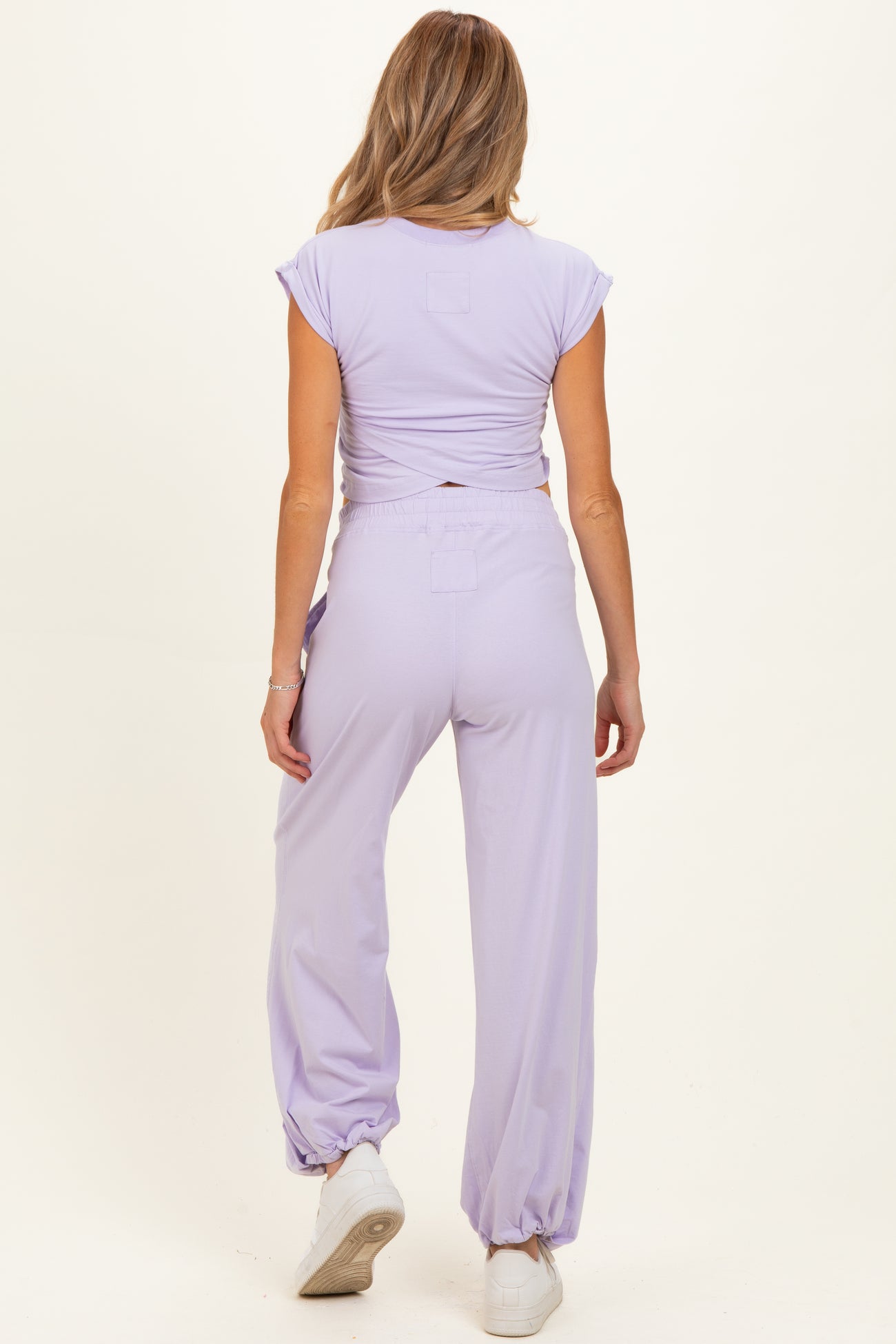 woman wearing a lilac maternity two-piece outfit with a cropped top and high-waisted pants, showing a baby bump